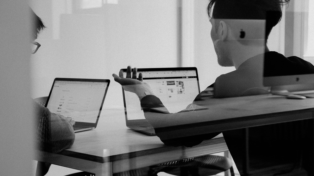 Business meeting between two professionals evaluating custom software vendors on laptops.