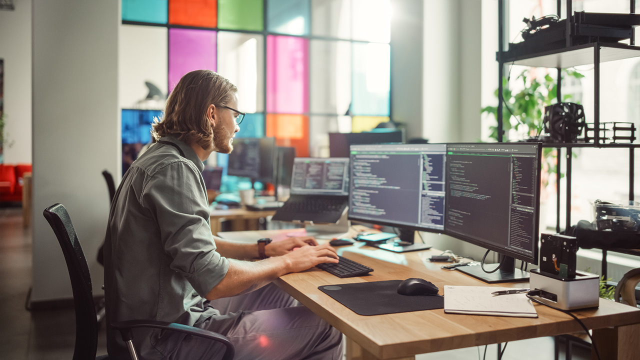 In-house software engineer coding on dual monitors in a tech office environment.