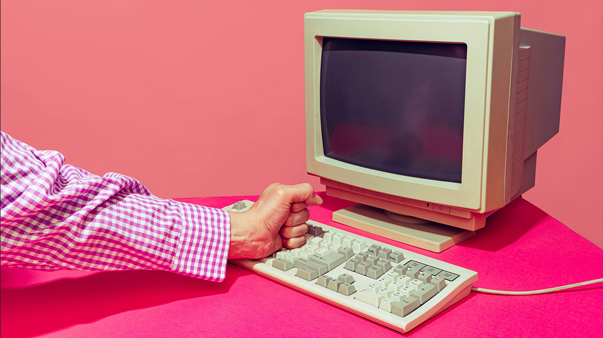 Frustrated person hitting an old computer keyboard, symbolizing the consequences of outdated systems and poorly planned software migrations.